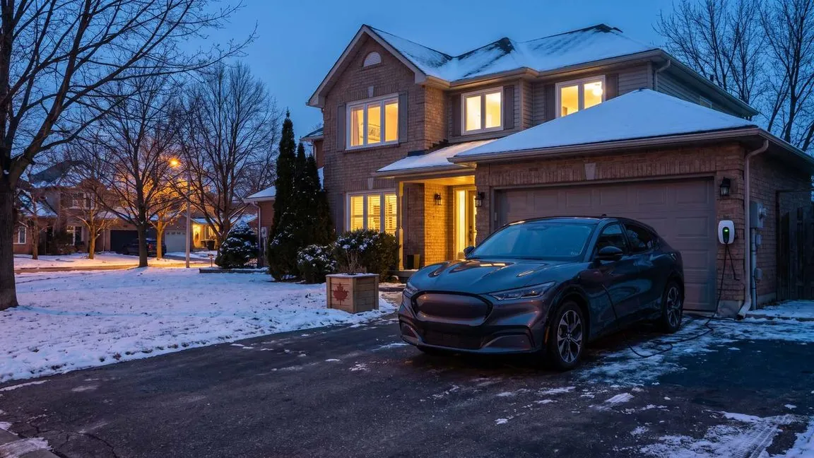 Electric SUV charging at a home charger in a snowy Canadian driveway at dusk